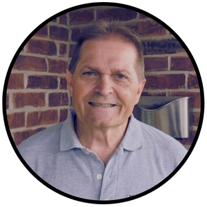 Photograph of Charles wearing a grey polo shirt standing in front of a red brick wall.
